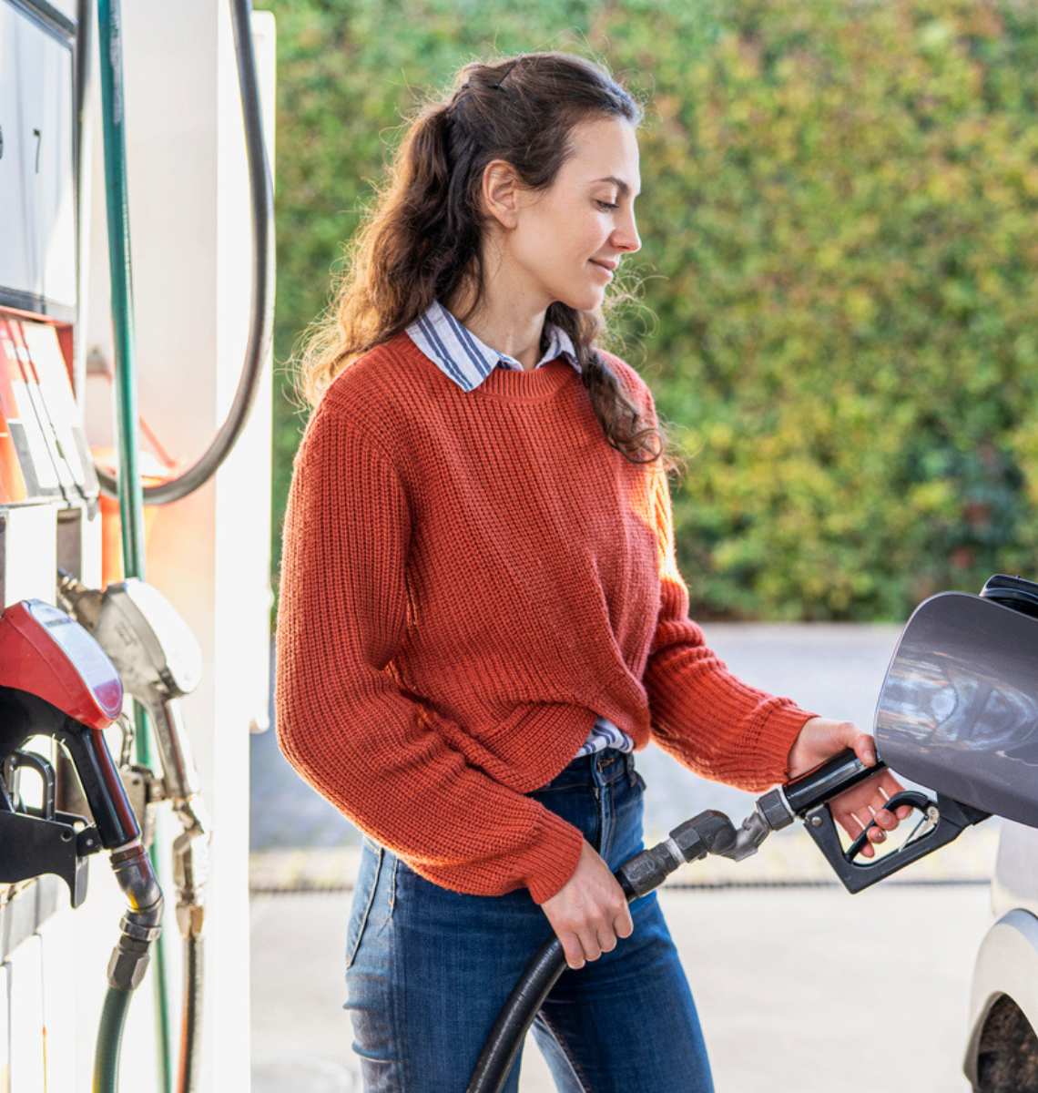 Young woman fueling her vehicle at a gas station.