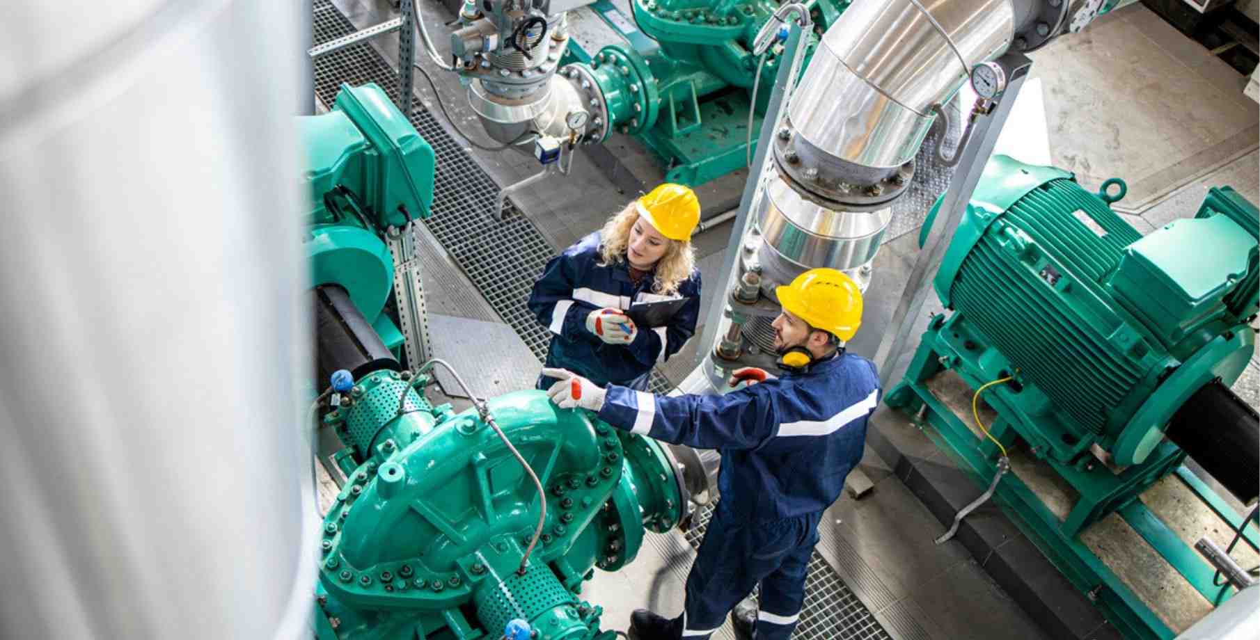 Two service provider workers in a large facility wearing safety gear.